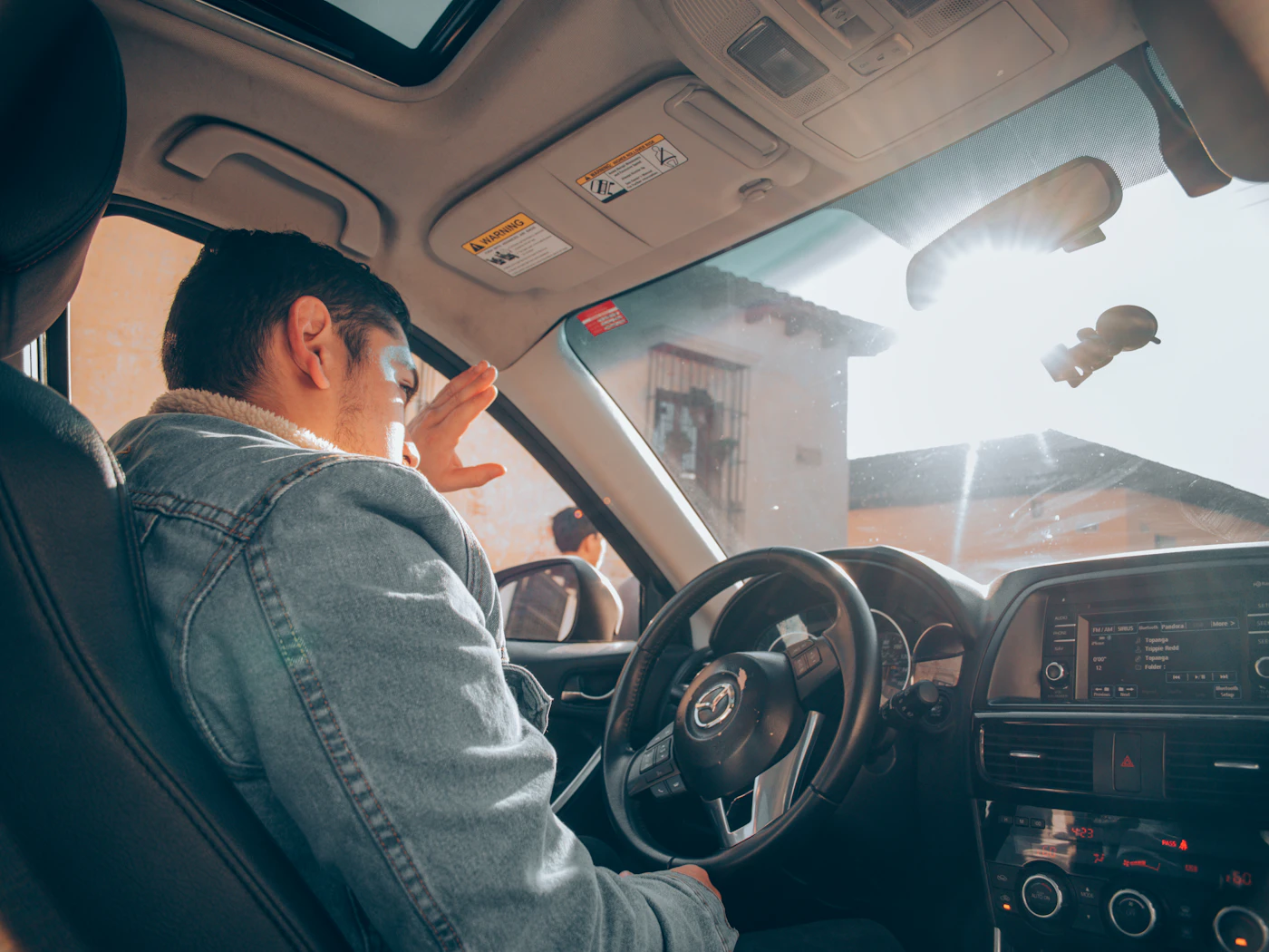 A driver shielding his eyes from low afternoon sun through the windshield